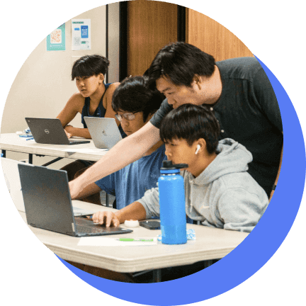 A coach working one-on-one with students at their laptops
